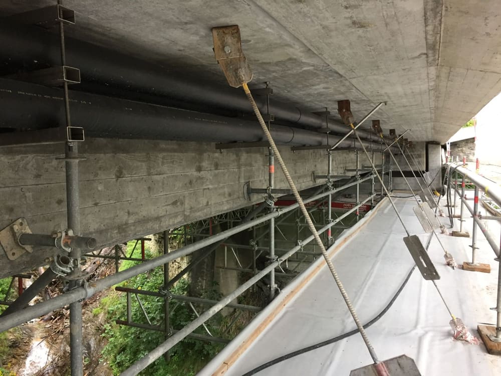 Unter der Brücke: Hängegerüst und Kabelschutzrohre, die an der Unterseite der Fahrbahnplatte aufgehängt sind