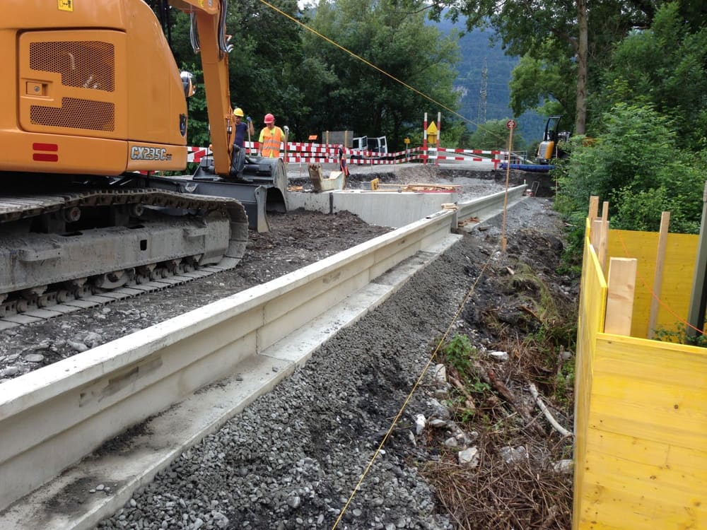 Kleintiermauer im Bau: Betonelemente der Leitwand auf Kiesbett, daneben der Bagger, im Hintergrund die abgesperrte Strasse