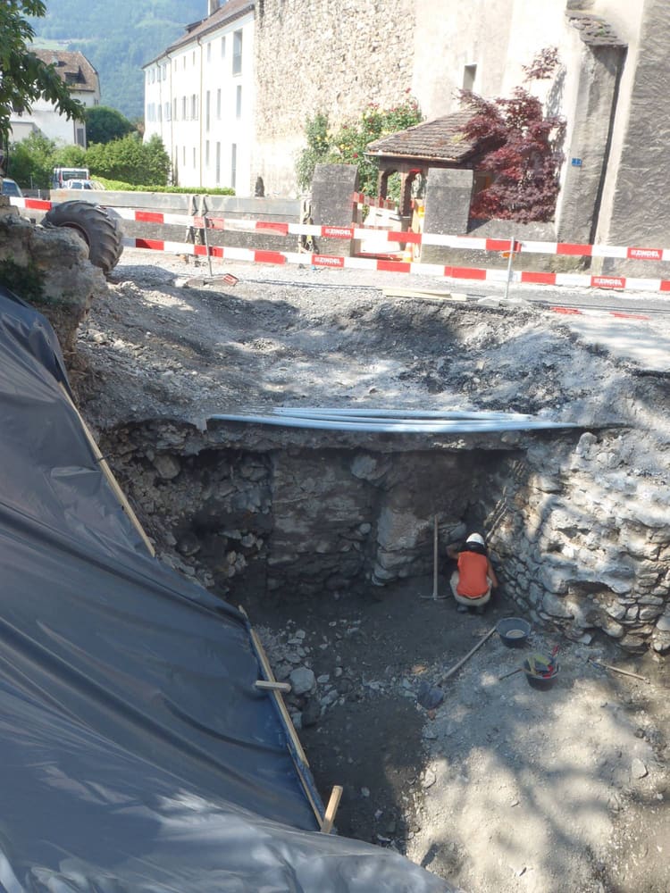 Archäologische Grabung beim Durchgang: Baugrube mit Mauerresten, oben die provisorisch gesicherten Leitungen
