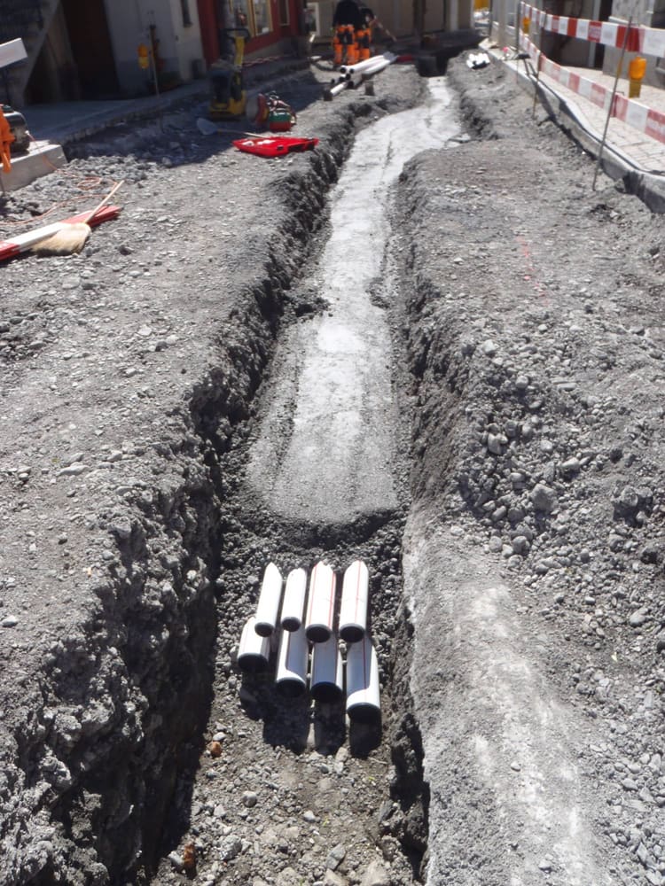 Leitungsgraben in der Gasse mit neuen Kabelschutzrohren, im Hintergrund die Baustelle