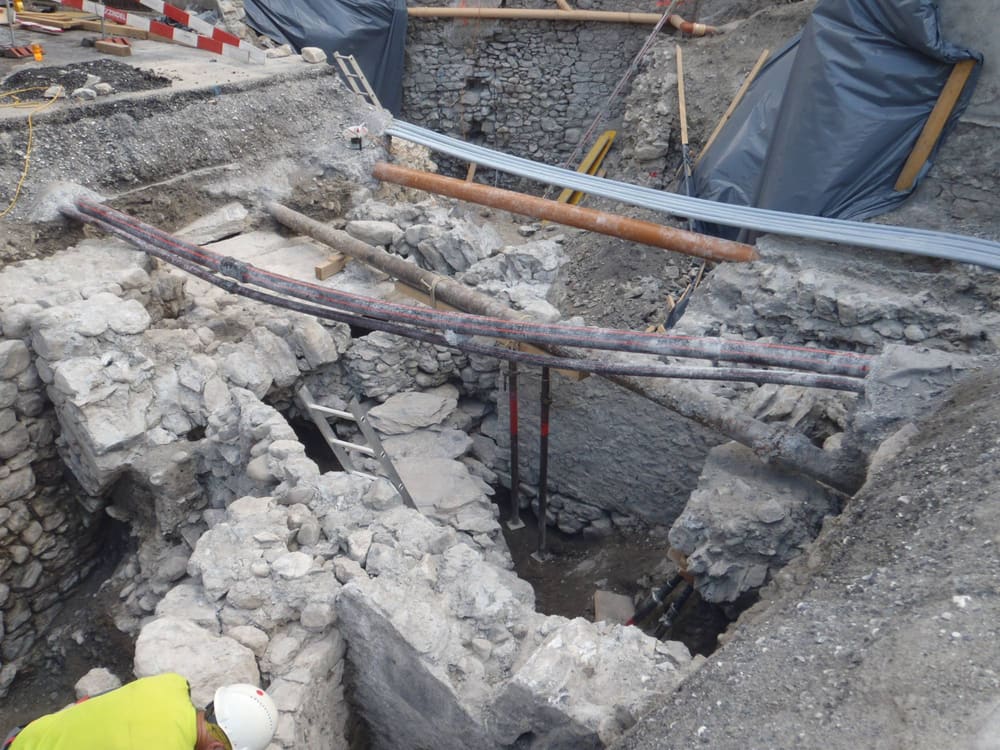 Archäologische Untersuchung in der Baugrube: freigelegte historische Mauern, darüber provisorisch geführte Leitungen