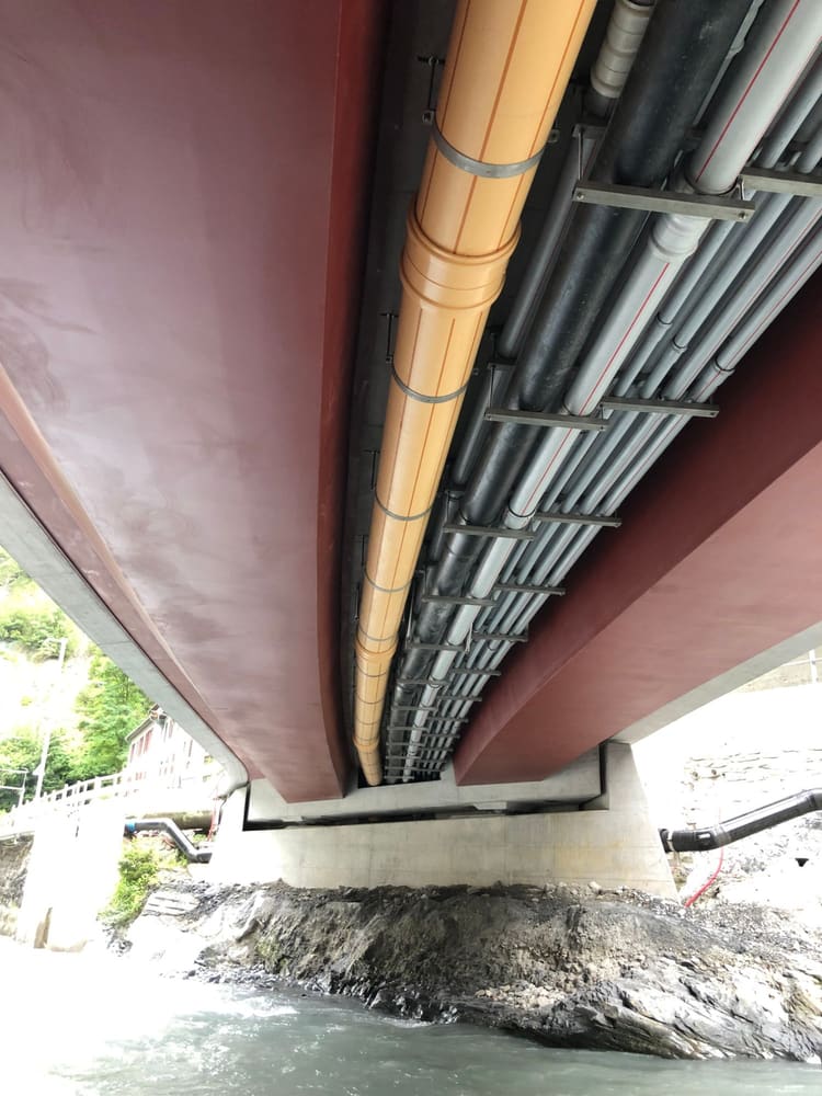 Untersicht der neuen Brücke: zwischen den beiden rot beschichteten Hohlkastenträgern hängen Kanalisation, Wasserleitungen und Kabelschutzrohre